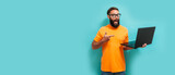 Fototapeta  - Young crazy bearded charismatic man. Shocked or surprised expression. Laptop concept. Funny promotion poster. Programmer, web developer holding a laptop in his hands and looking at the camera