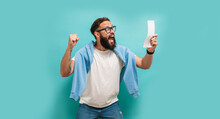 Excited Happy Young Male Winner Feeling Joy Winning Lottery, Placing Bets, Getting Cashback Online Gift Isolated On Blue Background. Human Face Emotions And Betting Concept. Trendy Colors