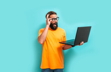 Young crazy bearded charismatic man. Shocked or surprised expression. Laptop concept. Funny promotion poster. Programmer, web developer holding a laptop in his hands and looking at the camera