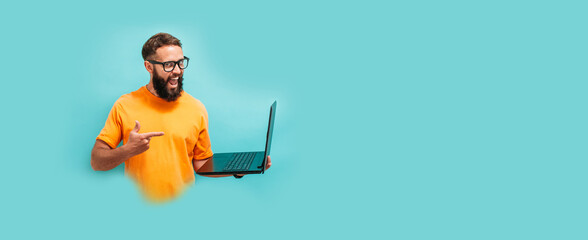 Young crazy bearded charismatic man. Shocked or surprised expression. Laptop concept. Funny promotion poster. Programmer, web developer holding a laptop in his hands and looking at the camera
