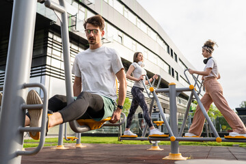 Group of friends man and women male and young adult people training at outdoor open gym in park in front of modern building real people sport and recreation exercise healthy lifestyle concept