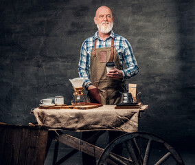 Studio shot of old fashioned elderly barman with mobile coffee shop against dark background.