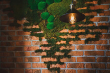 Retro Vintage Incandescent Lamp In A Stylish Loft Interior Against The Background Of A Brick Wall Covered With Moss