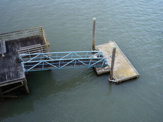 Wall Mural - Floating concrete jetty with metal bridge and wooden piles. Aerial view. Stock photo.