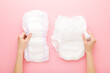 Young adult woman hands holding white big size sanitary towel and diaper pant on pastel pink background. Closeup. Hygiene product for urinary incontinence or after childbirth. Top down view.