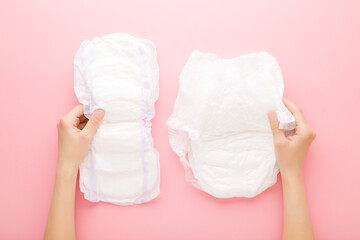 Wall Mural - Young adult woman hands holding white big size sanitary towel and diaper pant on pastel pink background. Closeup. Hygiene product for urinary incontinence or after childbirth. Top down view.