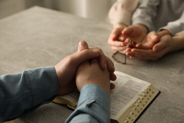 Boy praying and reading Bible with his godparents at grey table indoors, closeup