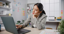 Young Asian Businesswoman Sit On Desk With Laptop Overworked Tired Burnout Syndrome At Office. Exhausted Lady With Sleeply Eye At Workplace, Girl Not Enjoy Unhappy With Work, Work Mental Health.