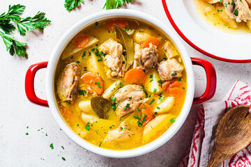 Chicken stew with potatoes and carrots in red saucepan. Chicken soup with vegetables and herbs. Comfort food recipe.