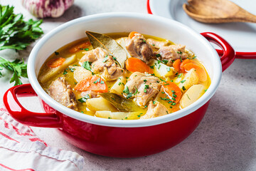 Wall Mural - Chicken stew with potatoes and carrots in red saucepan. Chicken soup with vegetables and herbs. Comfort food recipe.