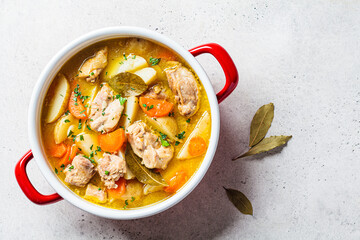 Wall Mural - Chicken stew with potatoes and carrots in red saucepan. Chicken soup with vegetables and herbs. Comfort food recipe.