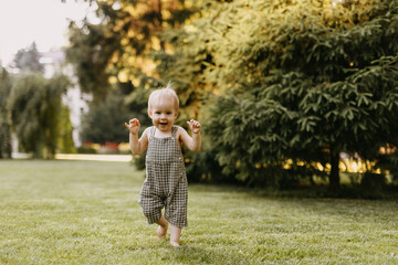 Wall Mural - Baby making first steps barefoot on freshly cut green grass in the park, smiling.