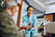 © Drazen - Young nurse assisting senior man in filling paperwork at doctor's office.