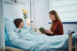 © Drazen - Caring mother reads book to her son during his recovery at hospital.