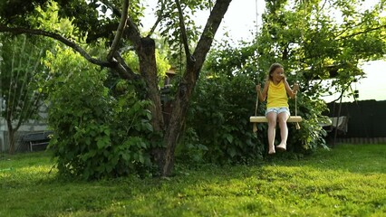 Wall Mural - Happy barefoot laughing child girl swinging on a swing in sunset summer day on the backyard at home, summertime outdoor, vacation.