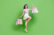 Full size photo of cute brunette lady hold bags jump wear glasses t-shirt skirt shoes isolated on green background