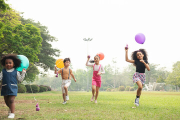 group of kids running in the spring field at public park with balloon. movement and blurry too soft.