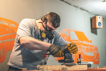 Male carpenter using orbital electric sander in a retro vintage workshop.