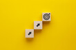 Wooden cubes with arrows and target icons on yellow background. Business development strategy, advancement and goal concept.