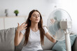 © Prostock-studio - Sad young european woman suffers from unbearably too hot weather, catches cold air from fan in living room