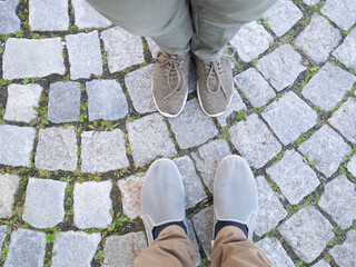 Two pairs of legs on paving stones.