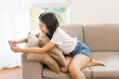 © Pichsakul - Home relaxation concept, Young woman sitting on couch and use smartphone to watching movie at home