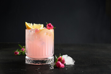 Wall Mural - Pink alcoholic cocktail with rose flowers on black background. Close up. Pouring freshness rose beverage or lemonade. Copy space.