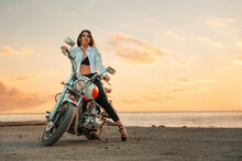 Sexy Woman With A High Heels And Leather Pants, Posing With Motorcycle. Sunset Sky On The Background. Copy Space. The Concept Of Motorcyclist Day