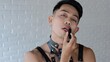 © Sia - The passionate face of a handsome homosexual man who paints his lips with lipstick. LGBT community for the rights of sexual minorities. Asian model male gay transgender looking at the camera.