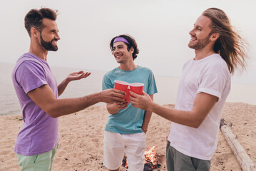 Poster - Photo of three cheerful friendly people hold plastic bear cup tell say toast communicate outside