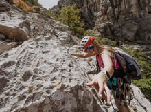 Athletic Woman In Protective Helmet And Harness With Rope And Quickdraws Climbing On Cliff Rock Wall Using In Paklenica National Park Site In Croatia. Active Extreme Sports Time Spending Concept.