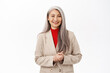 Portrait of stylish asian senior woman, looking confident, wearing blazer. Corporate businesswoman assisting, standing over white background