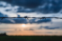 Silhouette Of Barbed Wire On A Fence Against A Cloudy Sky At Sunset.