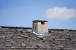 plastered chimney with cover on a roof with wood cover against a blue sky with clouds
