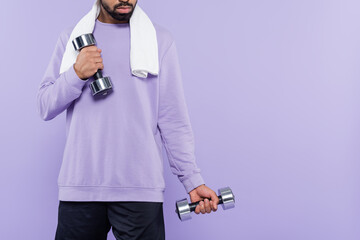 Wall Mural - cropped view of bearded african american man with towel exercising while holding dumbbells isolated on purple.