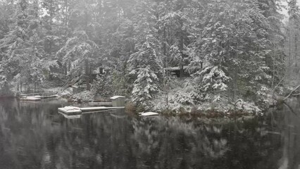 Wall Mural - Floating over a lake in winter with the snow falling and calm water.