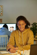 © DragonImages - Smiling schoolgirl listening to teacher during online class and taking notes in notepad