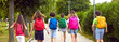 Children on their way to school. Group of little kids going to class. Six male and female students with colorful red, green, yellow, blue and pink backpacks walking along the park path. Banner, header