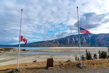 Canadian & American Flags Seen At Half Mast. Stunning Mountain Background With Blue Sky And Clouds. 