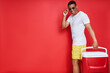 Handsome mixed race man carrying cooler box and smiling while standing against red background