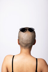 Wall Mural - Woman standing back to camera with shaved head and sunglasses on it in white studio background with copy space. Woman skin with suntan. One part of head covered in shadow. Model with small dark hair