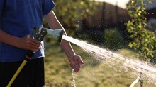 Child Plays With Water Hose Sprinkler In The Garden. Sunny Summer Day Children Playing In The Backyard. In Slow Motion