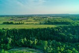 Fototapeta Na sufit - Aerial shot of green fields, forests and a creek bending in the foreground