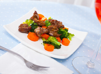 Wall Mural - Appetizing braised chicken hearts with vegetable garnish of steamed broccoli and carrots..