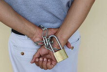 Man Hands Are Tied To Back With Metal Padlock And Steel Chain On Gray Wall Background Closeup.