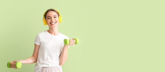 Sporty young woman with dumbbells listening to music on green background with space for text