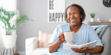 Happy Mature African-American Woman With Cup Of Tea And Book At Home. Concept Of Ageing And Menopause