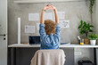 © Miljan Živković - One woman adult mature caucasian female at her office desk sitting at work stretching arms Relaxation exercise Resting while taking a brake Workplace Concept copy space real people back view