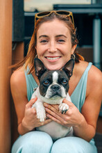 Portrait Of Smiling Young Woman Hugging Her Boston Terrier Dog In Front Of Camper Van