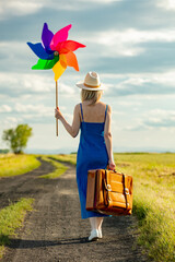 Canvas Print - Girl in blue dress with suitcase and pinwheel on country road in summer.